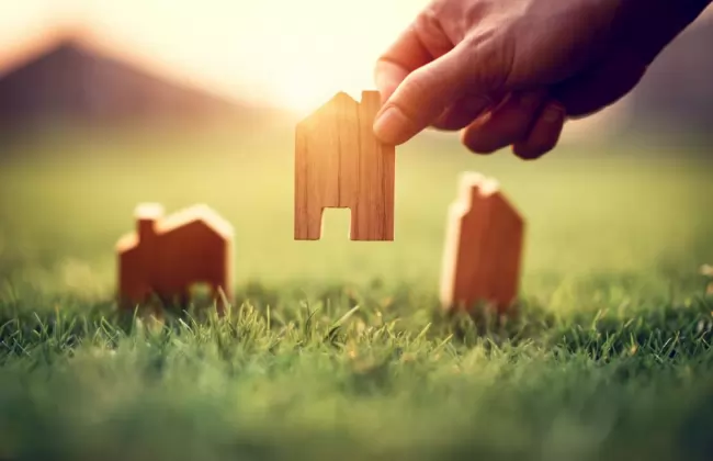 hand-of-woman-choosing-mini-wood-house-model-on-green-grass-planning-buy-real-estate-eco-house-icon-concept